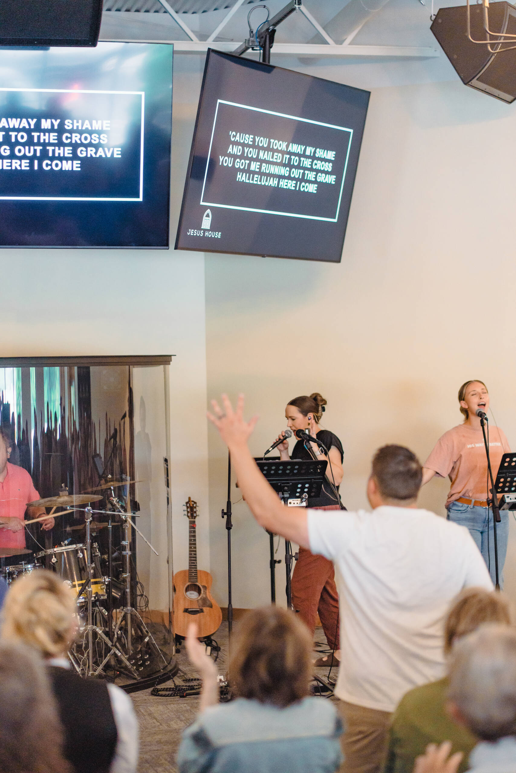 Worship band performing on stage in a church, with two screens displaying song lyrics and a cheering crowd in front.