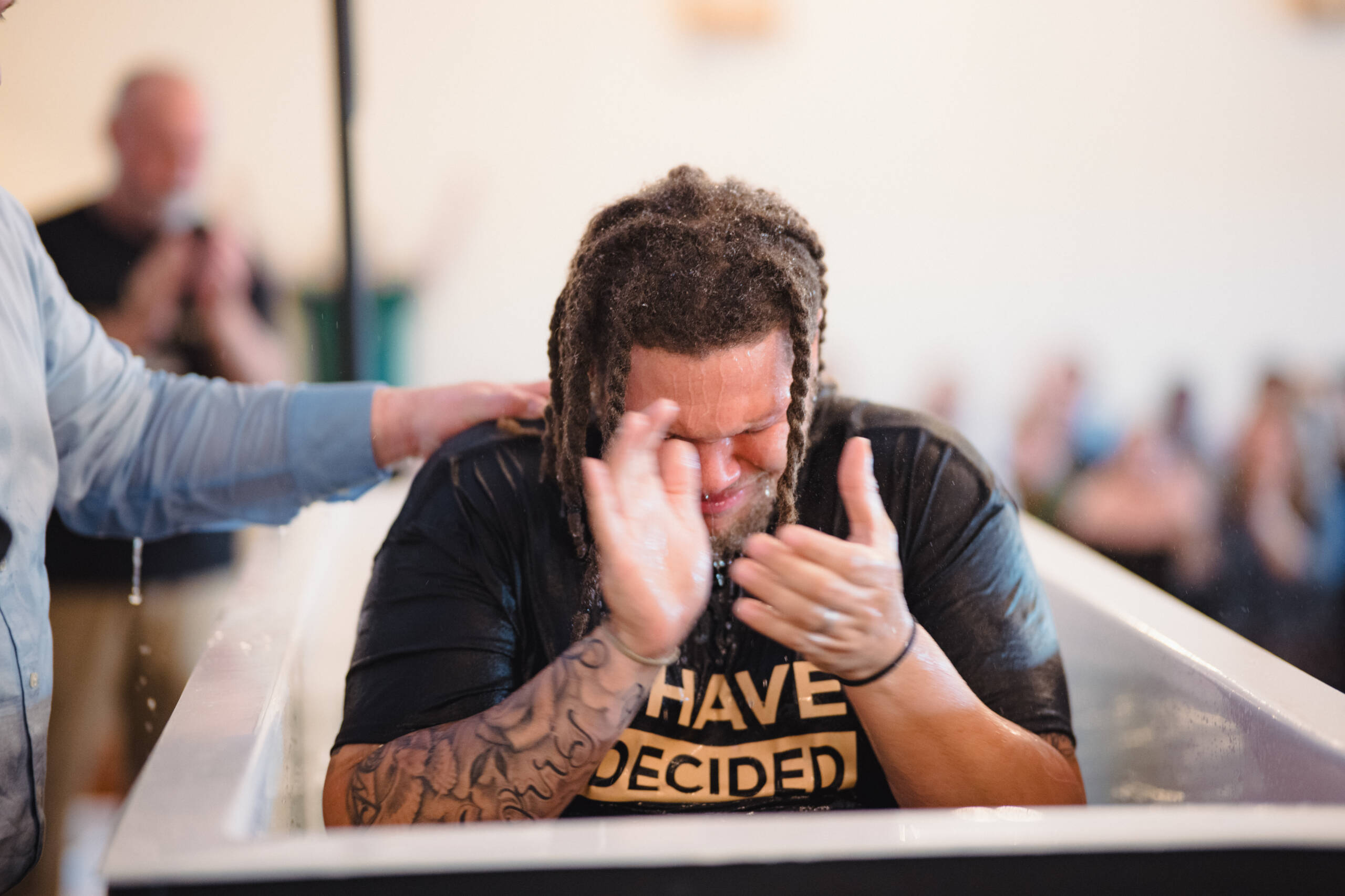 Person with braided hair washing their face at a sink, water splashing and hands raised.